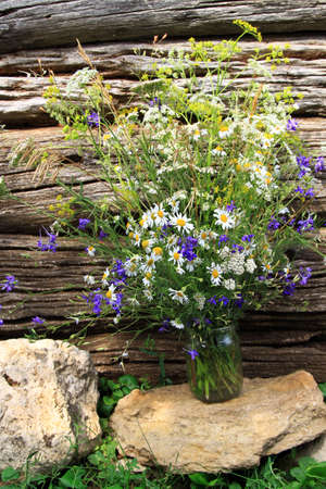 Bouquet of wildflowers in glass jar on stone with old wood backgroundの写真素材
