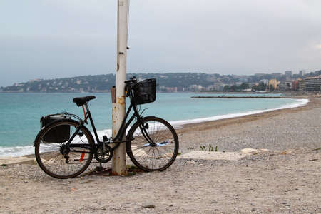 Lonely bicycle on beach on cloudy rainy day. Beach in Menton, town in South of France.の写真素材