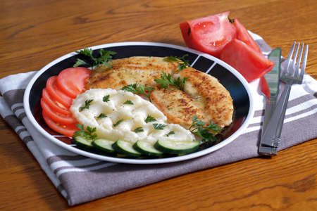 Fried tilapia fish fillets on plate with mashed potatoes, cucumber, tomatoes, parsley.の写真素材