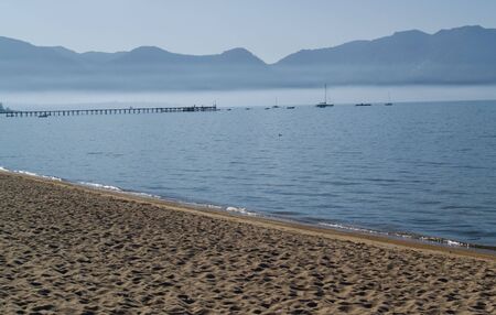 Lake shore with boats and pier in the background, mountains and fog in the distance.の写真素材