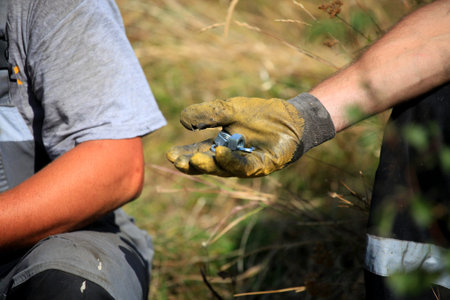 Two sitting workers outdoors closeup, one man holds nuts and washers in his gloved hand