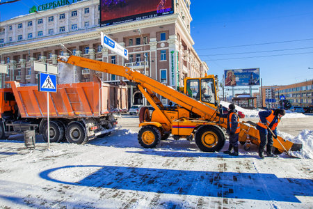 Snow removal works, snow removal tractor elevates snow in the truck with a help of two workers. Shot...