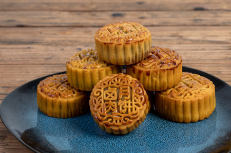 There are moon cakes on the plate of the wood grain table. The moon cakes are engraved with red bean...