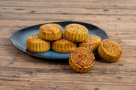 There are moon cakes on the plate of the wood grain table. The moon cakes are engraved with "red bean sand, marinated meat, egg yolk and strawberry moon cakes"の写真素材