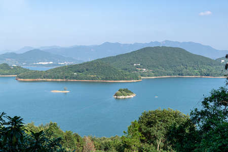 Under the blue sky, the lake is surrounded by mountains and forestsの写真素材
