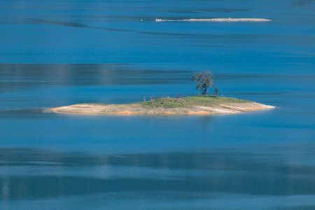 The shore of the lake is green, there are some small islands in the center, and the sky and water are blueの写真素材