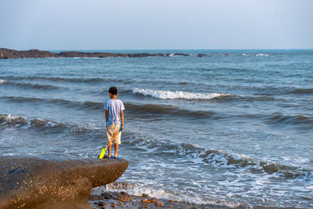 A child stood on a rock by the sea with an iron toy.の写真素材
