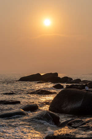 The beach under the setting sun is golden, and the people playing by the beach leave a silhouetteの写真素材