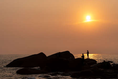 The beach under the setting sun is golden, and the people playing by the beach leave a silhouetteの写真素材
