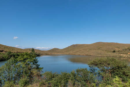 Under the blue sky, the natural lake on the meadow has yellow grass and blue waterの写真素材