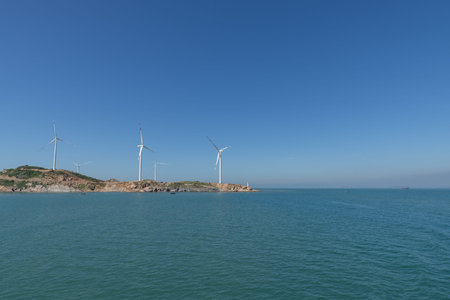 On the island in the middle of the sea, many wind turbines are installed under the blue skyの写真素材