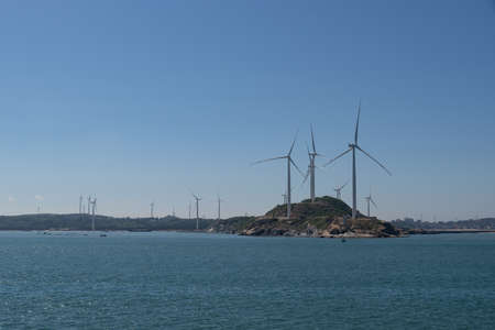On the island in the middle of the sea, many wind turbines are installed under the blue skyの写真素材