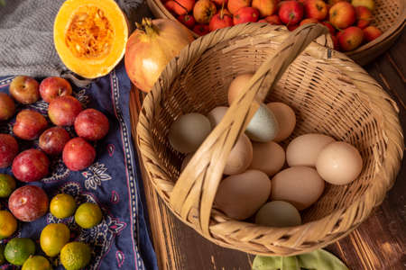 The eggs and other fruits and vegetables in the basket are on the wood grain tableの写真素材