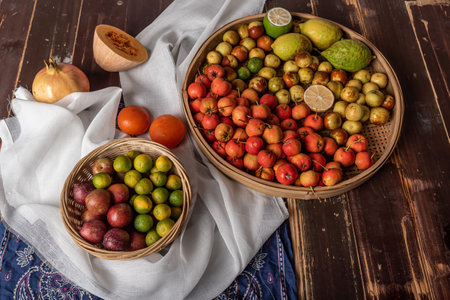 Many colors and varieties of fruit are either on the plate or scattered on the wooden tableの写真素材