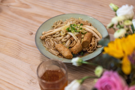 A bowl of noodle soup with sausage, vegetables and meat is on the table