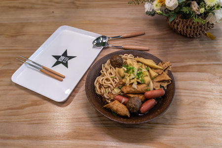 A bowl of noodle soup with sausage, vegetables and meat is on the table