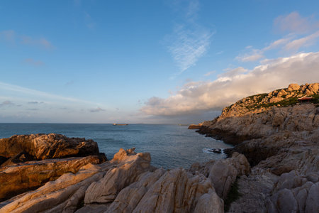 In the morning, the sun shines on the rocks and waves on the beach;の写真素材