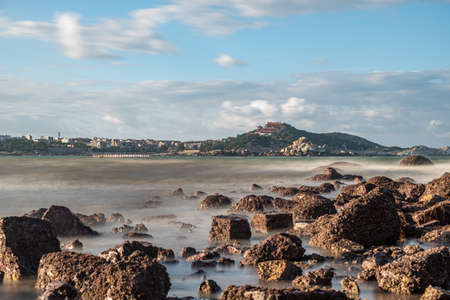 In the morning, the sun shines on the rocks and waves on the beach;の写真素材