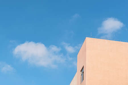Part of the light yellow building under the blue sky and white cloudsの写真素材