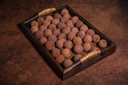 Dried litchi on a square plate on a dark yellow textured tableの写真素材