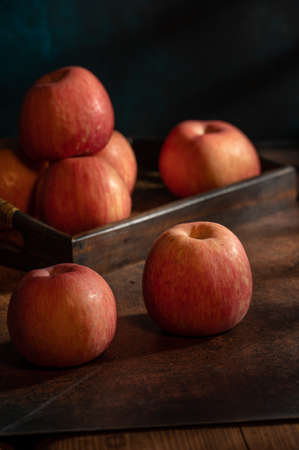 The apples on the plate look like oil paintings under the dim light on the wood grain tableの写真素材