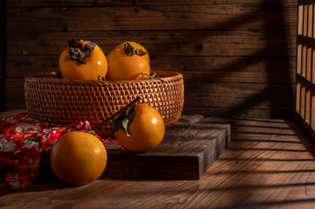 Persimmons on the plate are on the wooden table in dark lightの写真素材