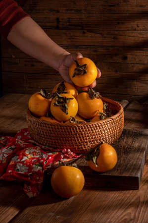 Persimmons on the plate are on the wooden table in dark lightの写真素材
