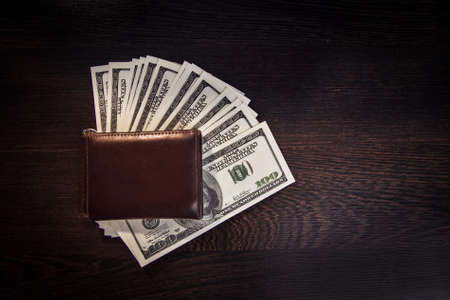 Money in a leather wallet on a dark wooden deskの写真素材
