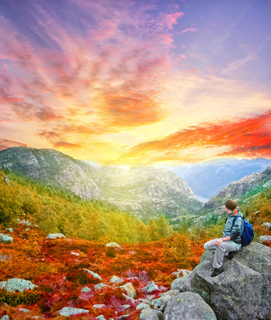 Woman traveler with backpack hiking in Norway mountains with magnificent waterfall. Beautiful autumn sunset landscape near Flam. Vintage style extreme travel backgroundの写真素材