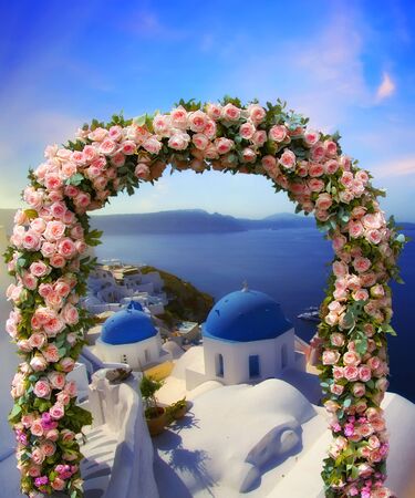 Wedding at Santorini. Beautiful arch decorated with flowers of roses with  blue church of Oia, Santorini, Greece at most romantic sunset in the world on the background. Wedding and honeymoon conceptの写真素材