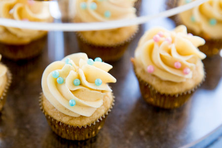 Vanilla bean mini cupcakes decorated with cyan and pink candy beads on a clear tiered tray up closeの写真素材