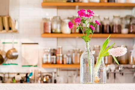 Flowers in two vases in a white kitchen with wooden shelves stocked with spicesの写真素材