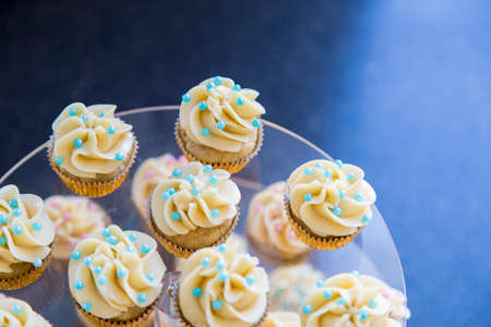 Vanilla bean mini cupcakes decorated with cyan and pink candy beads on a clear tiered tray up close.の写真素材