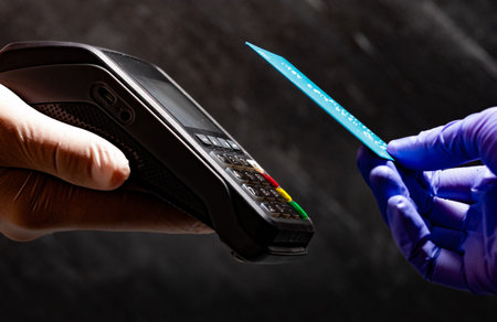 Paying contactless whit bank card at POS with medical gloves on black background.