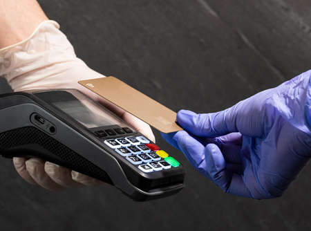 Paying with a gold card contactless at POS with medical gloves on black background.の写真素材