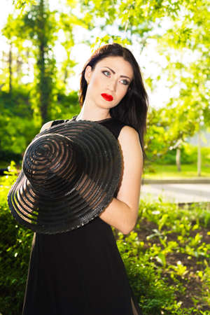 Portrait of attractive young brunette  woman keeping her hat in the hands in the parkの写真素材