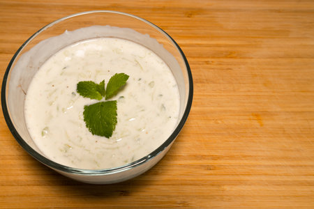Bowl of cucumber yoghurt salad dressing on wooden backgroundの写真素材