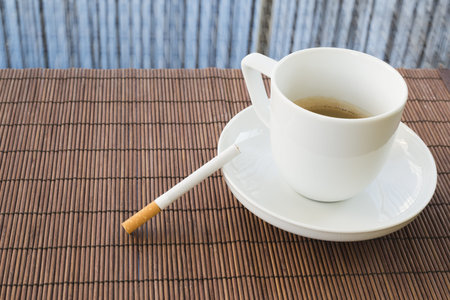 Cup of coffee and cigarette composition over a straw mat background