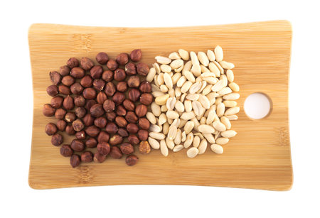Wooden cutting board covered with hazelnuts and peanuts isolated over white background