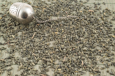 Metal tea infuser on scattered black tea over bamboo mat