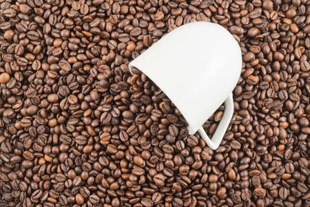 Coffee beans spilled out of white ceramic cup as abstract background, top viewの写真素材