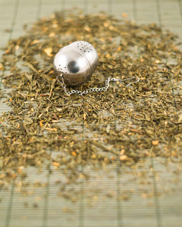 Metal tea infuser on scattered green tea over bamboo matの写真素材
