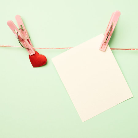 Heart and empty copyspace greeting card attached with a clothespin over a mint green background