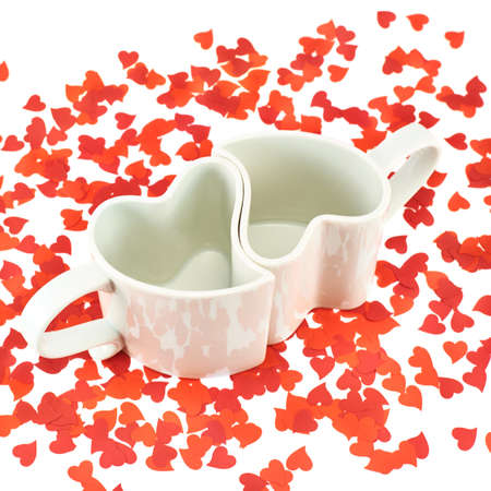 Two hearts shaped ceramic cups composition among red heart confetti over the white backgroundの写真素材
