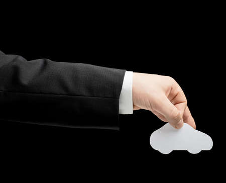 Caucasian male hand in a business suit, holding the white paper car shape, low-key lighting composition, isolated over the black backgroundの写真素材