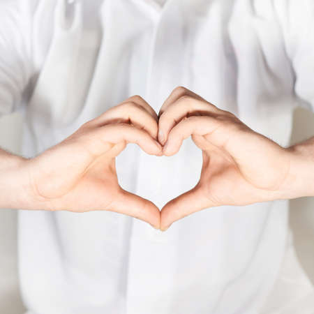Two hands gesture forming a heart shape against the white shirt, shallow depth of fieldの写真素材