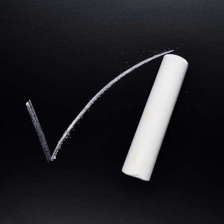 Drawn on the black blackboard white yes tick sign next to a piece of chalkの写真素材