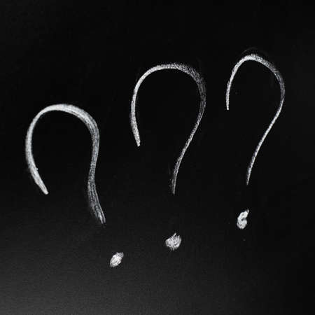 Three question marks drawn with the chalk on the black blackboardの写真素材