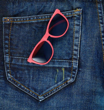 Red sun glasses in a back pocket of a navy blue denim jeans as a background compositionの写真素材