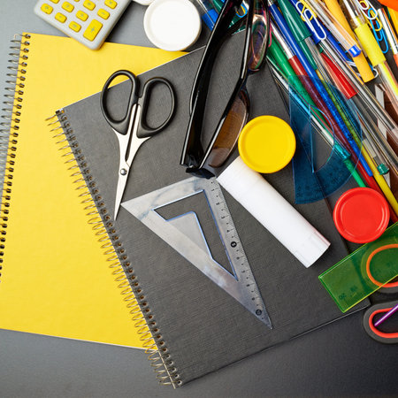 Black desk\'s surface covered with multiple stationery office supplies as a background back to...